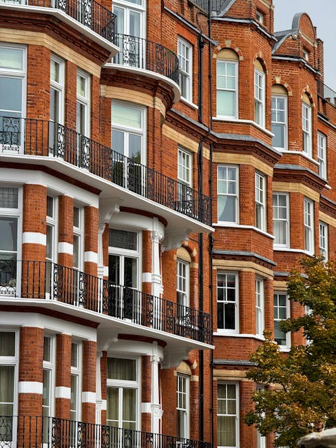 A multi-storey red brick residential building in South Kensington with curved bay windows and ornate black wrought iron balconies on each floor. The building features white decorative horizontal bands